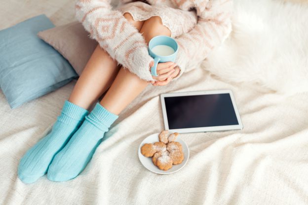 Soft photo of woman on the bed with tablet and cup of milk in hands, top view point