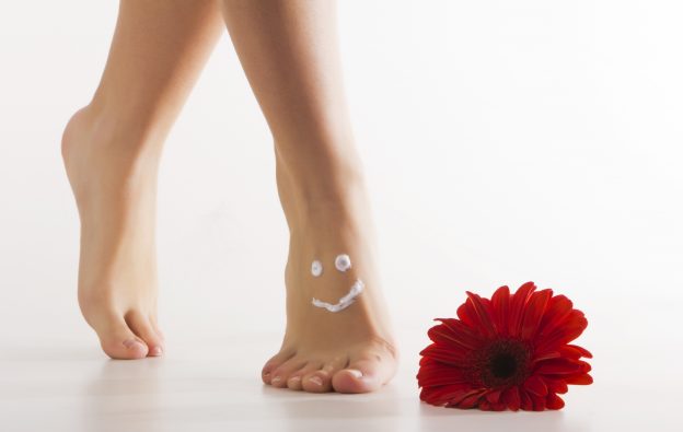 A woman, standing on her tiptoes next to a red flower, with a smiley face drawn on her feet.
