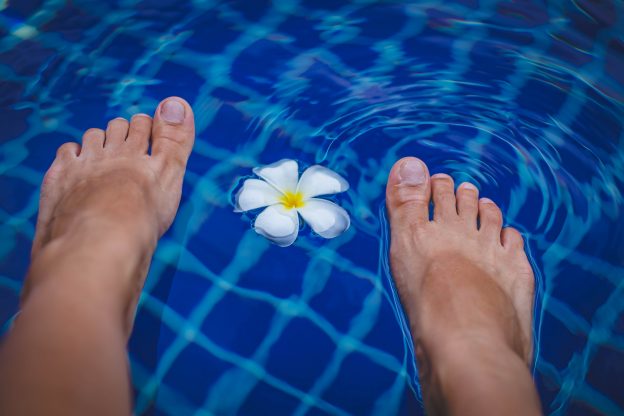 A person dips their feet in a pool near a flower