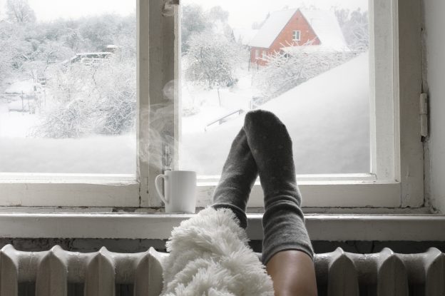 A pair of feet in warm socks sit near a window with a winter scene outside